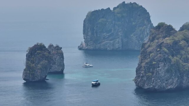 Catamaran and tour boat cruising vibrant turquoise waters of the Andaman Sea, surrounded by dramatic limestone karst islands and tropical nature in Koh Lanta, Thailand. Aerial drone shot panorama
