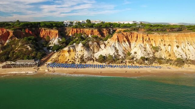Scenic aerial view flying over the stunning praia da falesia beach, a beautiful coastline bordered by spectacular ochre colored cliffs with pine trees on top in algarve, portugal