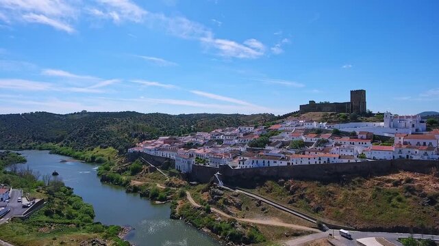 Stunning aerial perspective capturing the historic town of mertola, with its ancient castle and traditional white houses perched above the serene guadiana river in the alentejo region of portugal