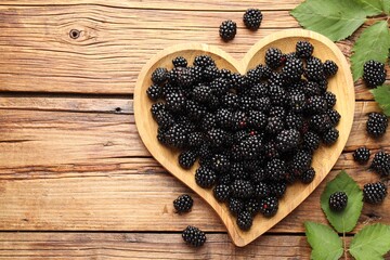 Naklejka premium Ripe blackberries with leaves on wooden table, flat lay. Space for text
