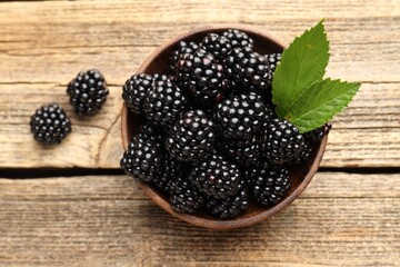 Ripe blackberries in bowl with leaves on wooden table, flat lay © New Africa