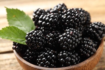 Ripe blackberries in bowl with leaves on wooden table, closeup © New Africa