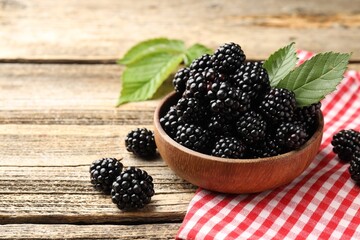 Ripe blackberries in bowl with leaves and towel on wooden table, closeup. Space for text © New Africa