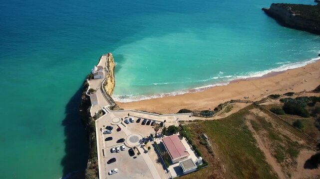 Drone footage slowly descending over the chapel of nossa senhora da rocha, a historic hermitage built on a scenic cliff overlooking the atlantic ocean and sandy beach in armacao de pera, algarve
