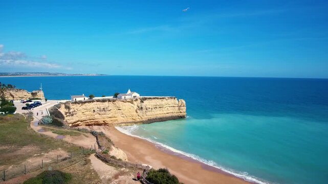 Majestic aerial view of the iconic chapel of nossa senhora da rocha perched on a cliff overlooking the turquoise atlantic ocean in the beautiful algarve region of portugal on a sunny day