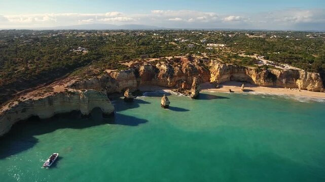 Spectacular aerial view of the iconic praia da marinha in portugal, with its golden cliffs and turquoise waters, as a tourist boat cruises along the stunning coastline of the algarve region