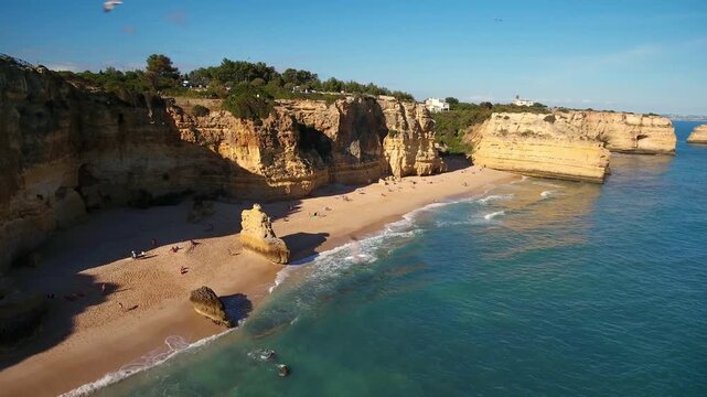 Aerial view flying along the stunning coastline of praia da marinha in the algarve region of portugal, revealing golden sand beaches, majestic sea stacks, and beautiful turquoise ocean waves