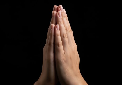 Closeup of two hands pressed together in a prayer position against a solid black background