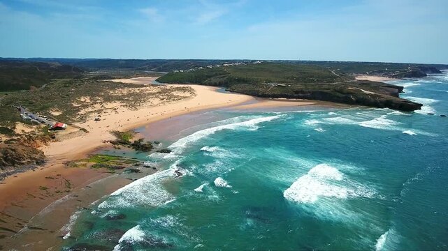 Sunny aerial perspective showing the stunning amoreira beach on the vicentina coast, with beautiful turquoise waves of the atlantic ocean crashing on the golden sand in aljezur, portugal