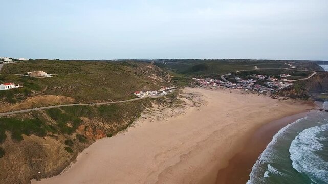 Dramatic aerial perspective of the vast sandy beach and charming village of monte clerigo, nestled along the rugged cliffs and powerful waves of the atlantic ocean on the costa vicentina