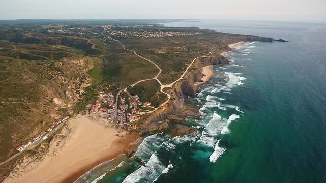 Breathtaking aerial view over aljezurs costa vicentina coastline showing monte clerigo village, sandy beach, dramatic cliffs and atlantic waves crashing on the shore