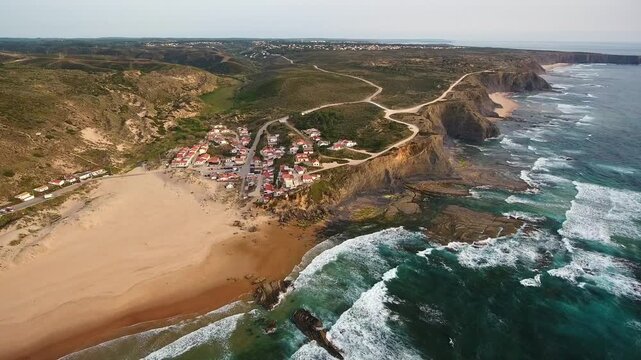 Drone view of the charming village of monte clerigo on the vicentine coast, featuring its sandy beach, rugged cliffs, and the powerful waves of the atlantic ocean crashing on the shore