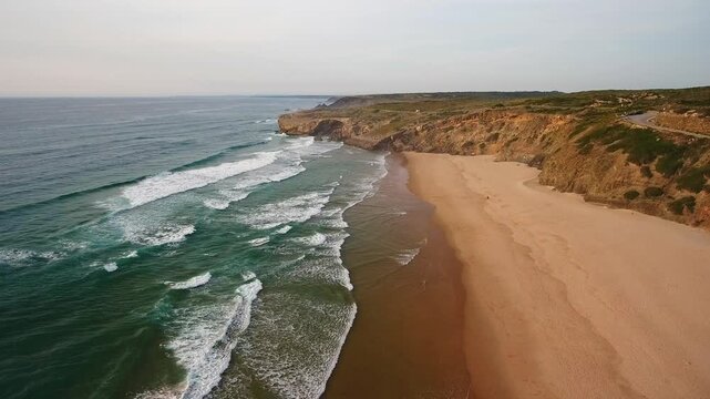 Stunning aerial perspective capturing the vast sandy shoreline and rolling waves of the atlantic ocean crashing onto praia de monte clerigo along the beautiful costa vicentina in aljezur, portugal