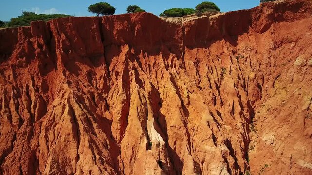 Drone footage ascending along the vibrant red and orange sandstone cliffs of falesia beach in algarve, portugal, revealing the beautiful and intricate patterns created by natural erosion