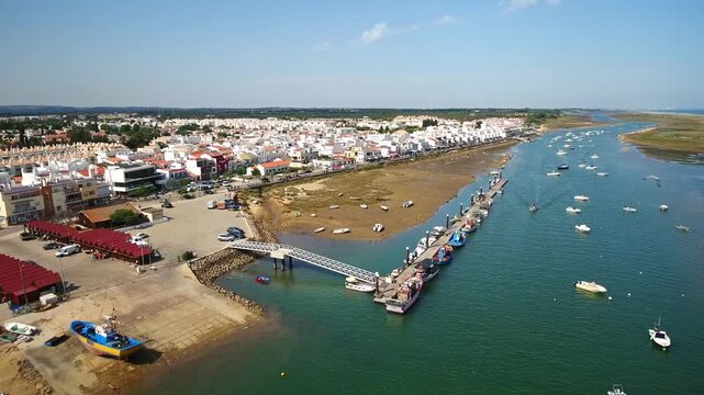 Drone flying over the scenic coastal village of cabanas de tavira in algarve, portugal, capturing the traditional white houses, bustling harbor, and boats floating in the ria formosa
