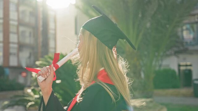 Woman holding diploma aloft and smiling in front of a building wearing mortarboard and red stole; pride achievement.