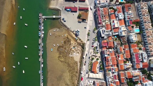 Zenithal aerial view slowly flying over the traditional fishing village of cabanas de tavira in the algarve region, revealing the beautiful houses and boats docked at the ria formosa lagoon