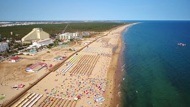Majestic aerial view showing the beautiful coastline of monte gordo in the algarve, with tourists enjoying the sun on the sandy beach and swimming in the calm, blue atlantic ocean