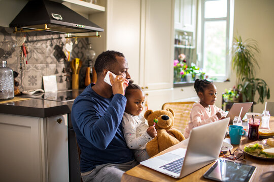 Father working from home with daughters in kitchen