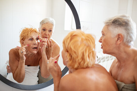 Two senior women applying skincare in bathroom mirror