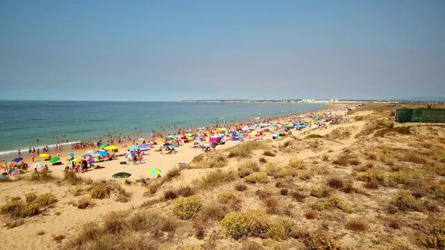 Sunny day at gale beach in albufeira, portugal, with numerous tourists enjoying the ocean, sunbathing under colorful umbrellas, and relaxing on the beautiful golden sand of the algarve coast