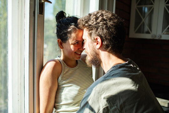 Young couple touching foreheads by sunny window at home