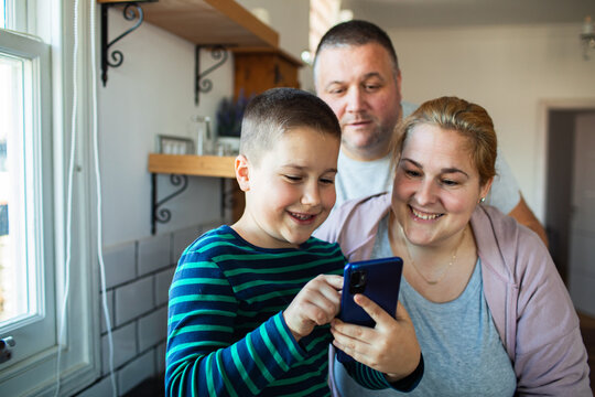 Parents and son using smartphone together at home kitchen