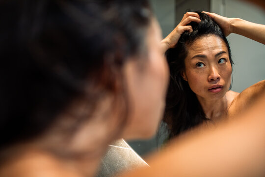 Woman checking scalp in bathroom mirror