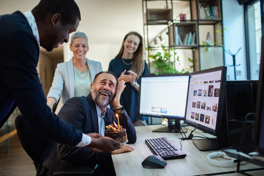 Coworkers surprise colleague with birthday cake at office desk