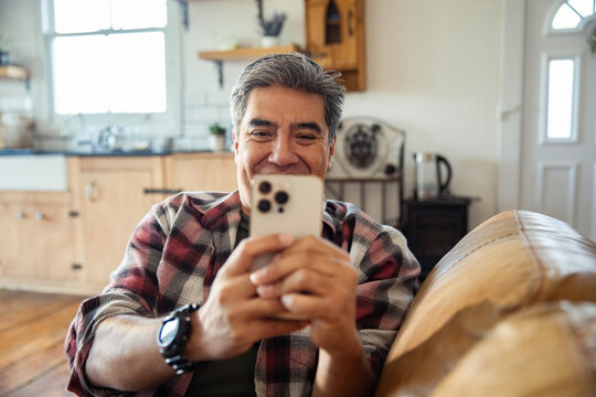 Smiling middle-aged man using smartphone on sofa at home