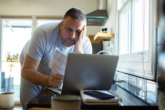 Stressed middle-aged man paying bills online in home kitchen