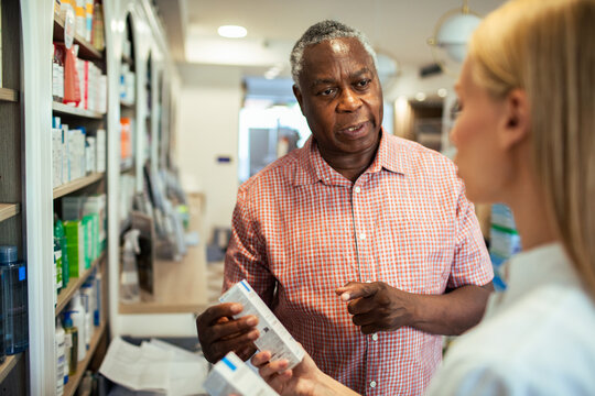 Senior man consulting pharmacist about medication in pharmacy