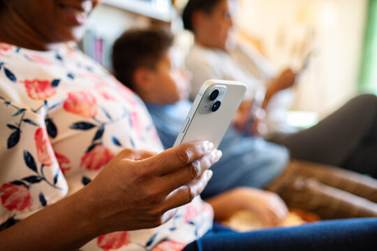 Close-up of woman using smartphone while family relaxes on sofa at home