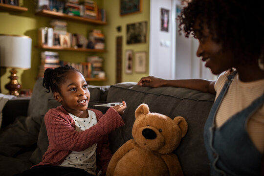 Girl checks teddy bear's temperature with mother at home