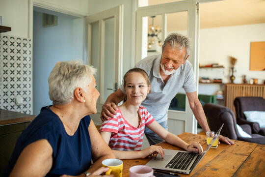 Grandparents helping granddaughter with homework on laptop at home