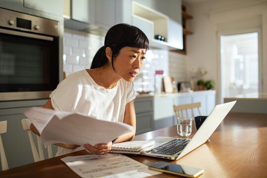 Woman reviewing household bills on laptop at kitchen table