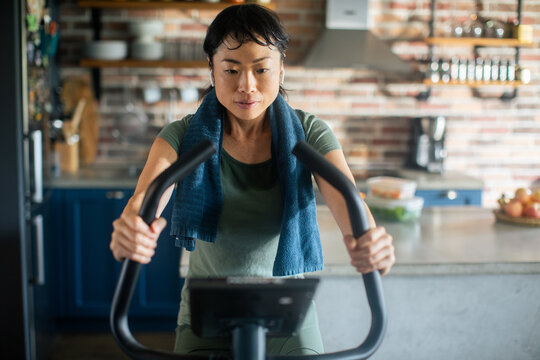 Focused woman riding exercise bike in home kitchen