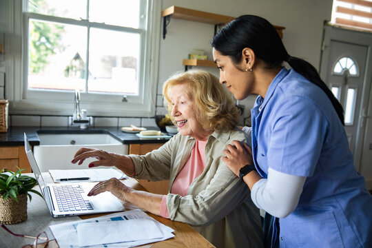 Caregiver helps senior woman use laptop in kitchen