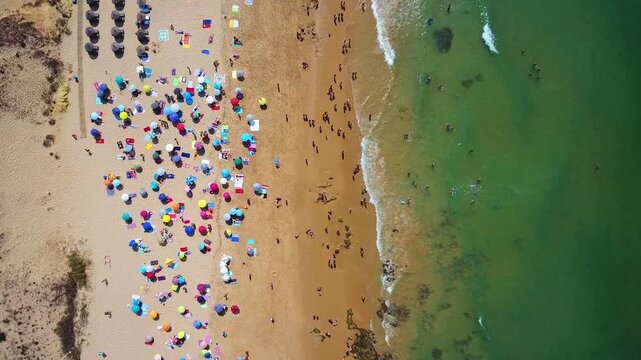Bird's eye view of a crowded tropical beach with colorful umbrellas, sunbathers and swimmers in green blue waves on a sunny summer day at a popular resort coastline
