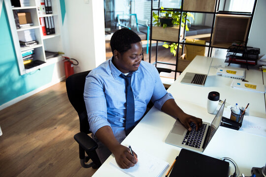 Office worker taking notes while using laptop in modern coworking space