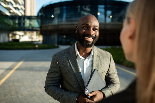 Smiling businessman holding tablet talking with colleague outside office