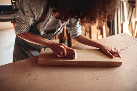 Close-up of carpenter sanding wood plank in workshop
