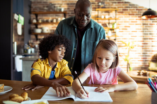 Senior man helping kids with homework at kitchen table