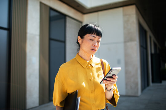 Businesswoman checking smartphone outside office building