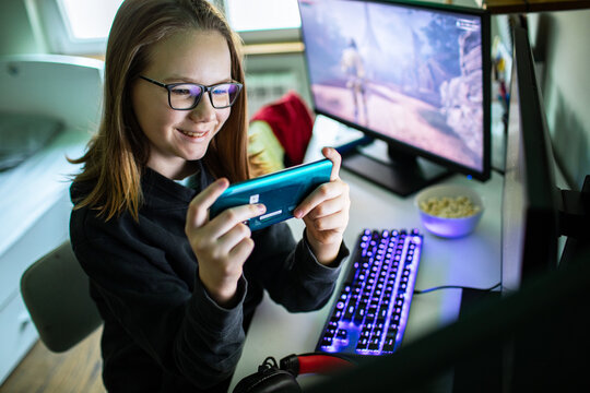 Smiling teen girl gaming on smartphone at home desk
