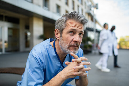Worried male healthcare worker in scrubs outside hospital