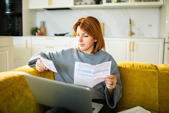 Woman reviewing bills with laptop on sofa at home