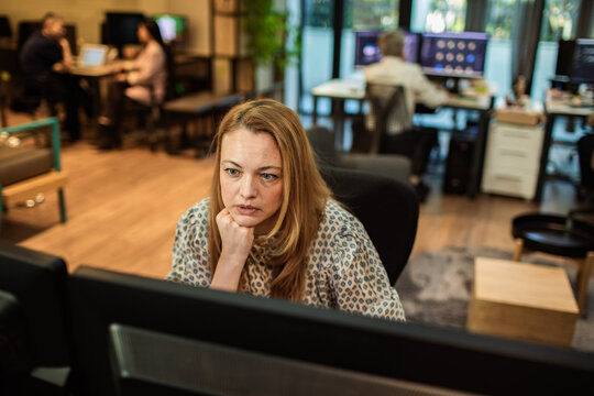 Focused woman working at dual monitors in modern open office