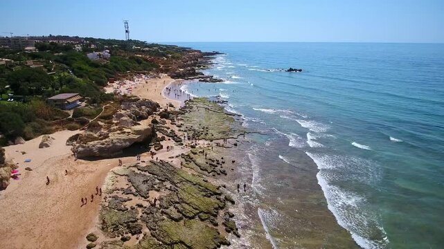 Aerial view of tourists exploring the scenic coastline with sandy beaches, rock formations, and clear blue water at praia da gale in albufeira, a popular summer travel destination in portugal