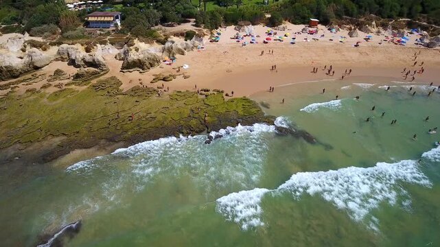 Aerial view flying away from the stunning gale beach in albufeira, portugal, where tourists enjoy sunbathing on the golden sand and swimming in the calm atlantic ocean on a beautiful summer day
